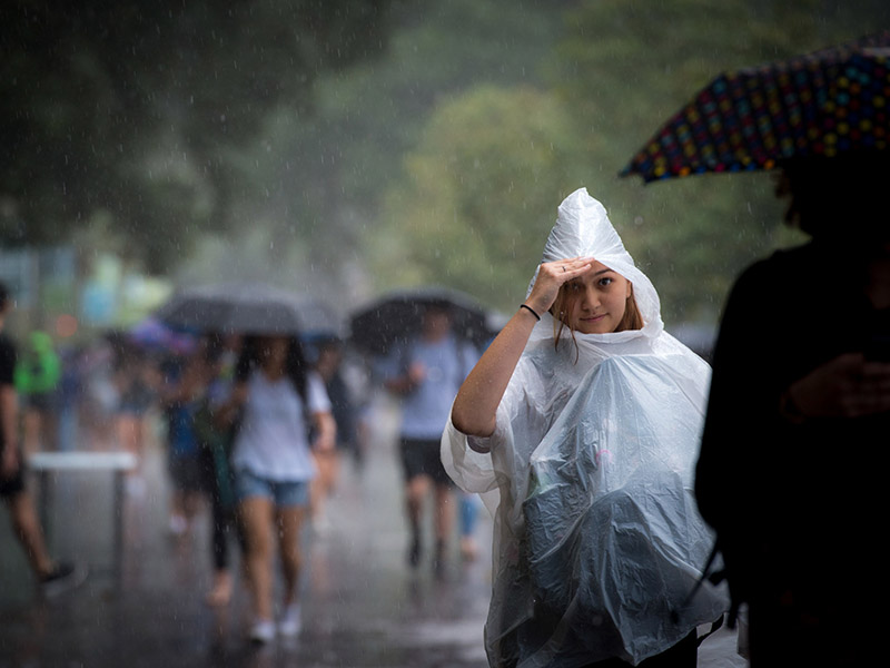 A Tulane senior peeks out from the protection of her rain poncho as she walks up McAlister Place during a downpour.